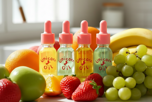 Four bottles of 'Unicorn Oil' with pink droppers on a table with fruits.