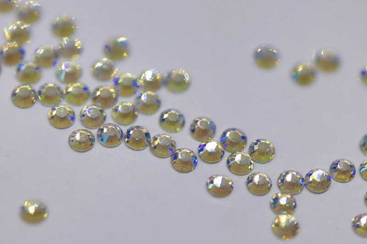 Bulk bag of Northern Lights SS6 (2.0mm) iridescent glass flatback rhinestones for professional nail art, showing green and blue shimmer.