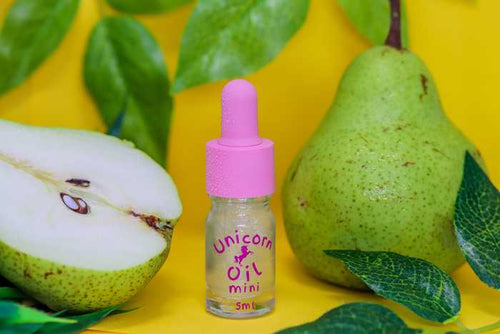 Bottle of 'Unicorn Oil Mini' with pears and leaves on a yellow background
