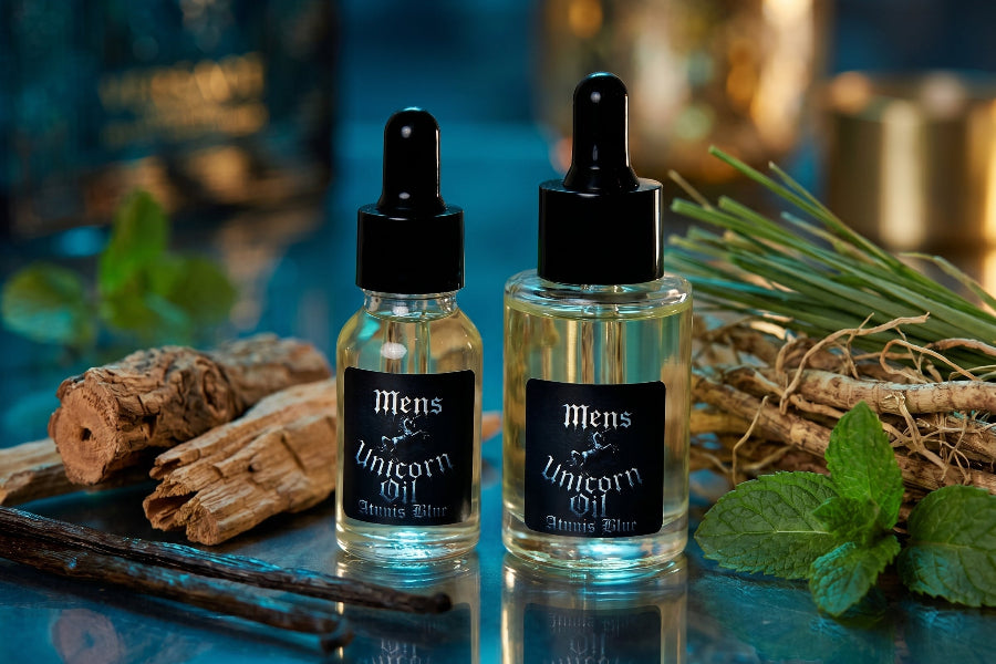 Two bottles of 'Mens cuticle Oil' on a reflective surface with herbs and wood.