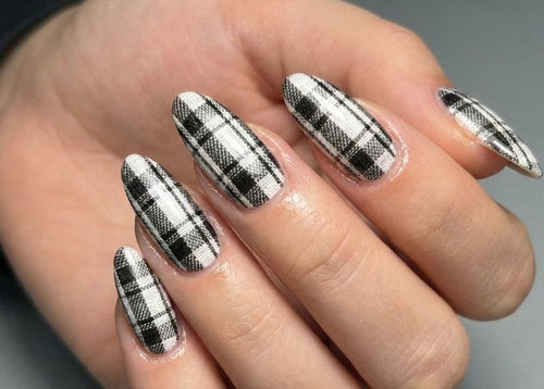 Hand with black and white plaid nail design on a neutral background