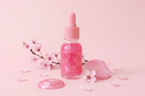 Pink bottle labeled 'Unicorn Oil' with cherry blossoms on a pink background