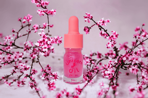 Pink cuticle oil dropper bottle labeled 'Unicorn Oil' with cherry blossoms in the background