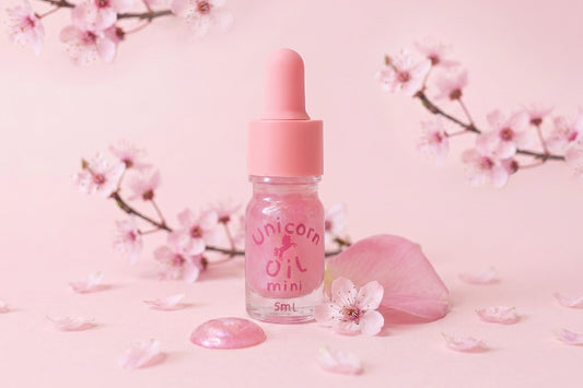 Pink bottle with dropper labeled 'Unicorn Oil' on a pink background with cherry blossoms.