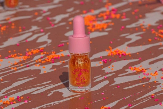 Small cuticle oil bottle with a pink dropper on a surface with colorful confetti