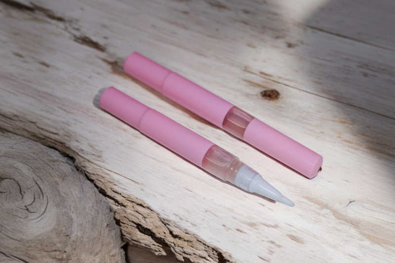 Two pink cuticle oil pens with clear accents on a wooden surface