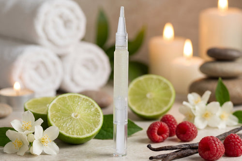 clear cuticle oil pen with limes, raspberries, vanilla beans, and candles on a neutral background
