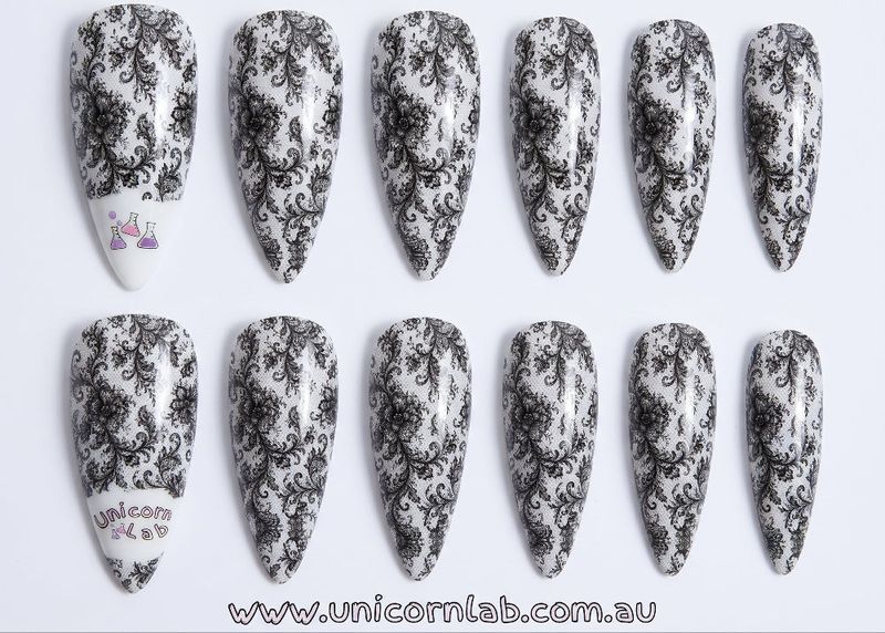 Set of stiletto-shaped nails with black floral patterns on a white background