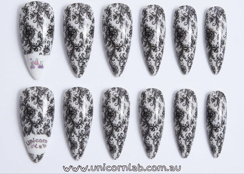 Set of stiletto-shaped nails with black floral patterns on a white background