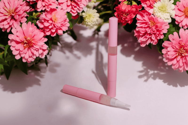 Floral Explosion Unicorn Cuticle Oil Pen in front of a bunch of pink flowers.