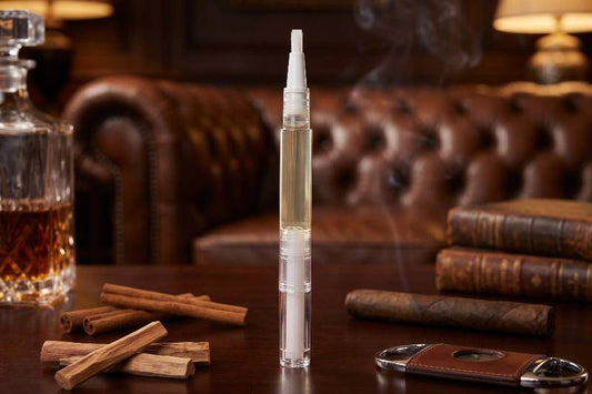 Mens Cuticle Oil pen on a wooden table with a glass of whiskey, cinnamon sticks, and books in the background.