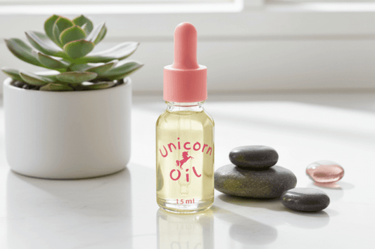 Bottle of 'Unicorn Oil' with a dropper on a white surface with stones and a plant.