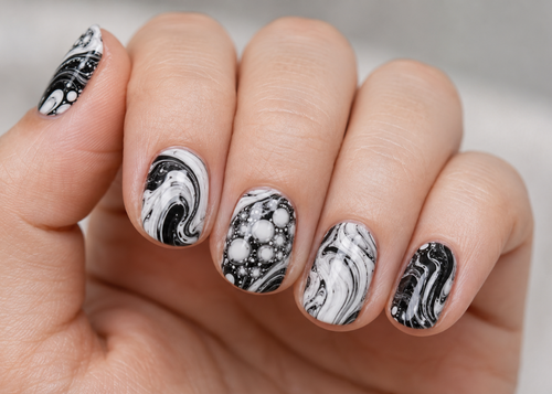 Hand with marbled black and white nail design on a neutral background