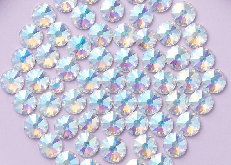 Collection of iridescent rhinestones on a light purple background.  SS12 Crystal Shimmer | Flatback Swarovski Crystals | 2088