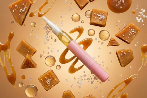 Pink salted caramel cuticle oil pen with caramel pieces and syrup on a gold background