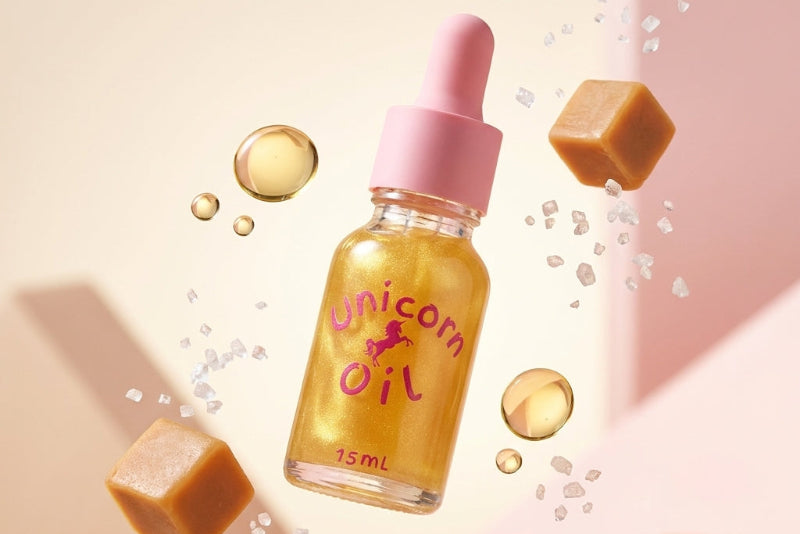Bottle of 'Unicorn Oil' with a pink dropper on a beige background. Salted Caramel Unicorn Cuticle Oil