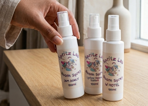 Three white spray bottles with labels on a wooden surface near a window.