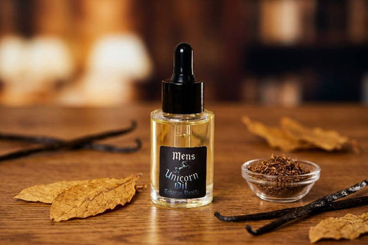Bottle of 'Mens Unicorn Oil' on a wooden surface with vanilla beans and leaves.