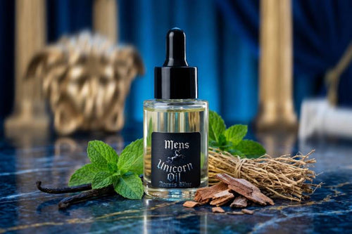 Bottle of 'Mens Unicorn Oil' with vanilla beans and mint leaves on a blue surface.