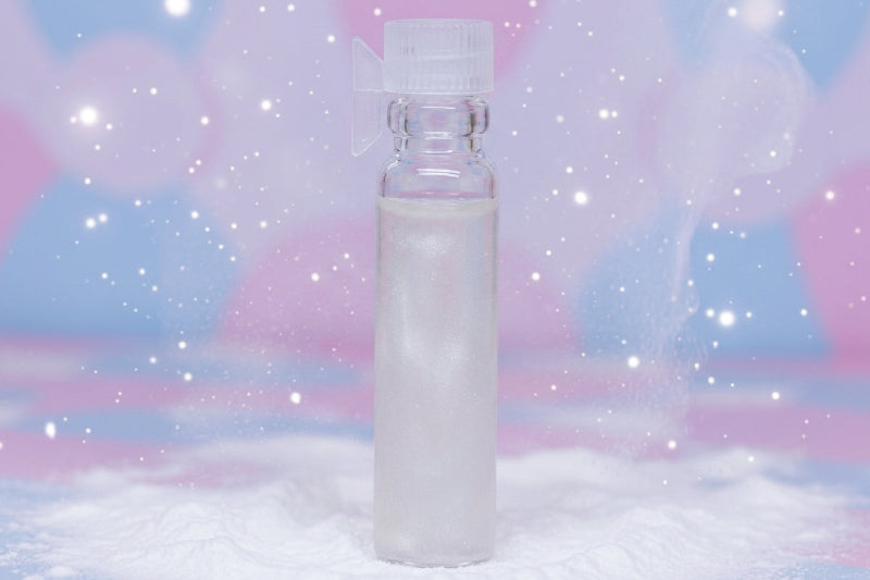 A small clear plastic bottle with a white cap stands upright on a white surface against a pastel pink and blue background with bokeh lights and white sparkles.