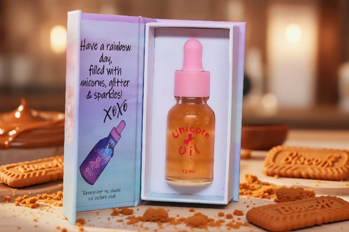 Unicorn oil bottle with pink cap in a decorative box on a table with cookies.