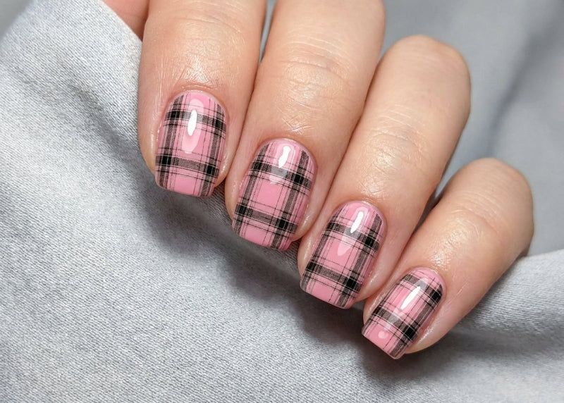 Nails with pink and black plaid design on a gray fabric background