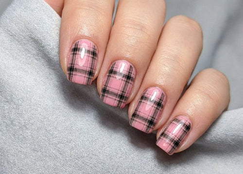 Nails with pink and black plaid design on a gray fabric background