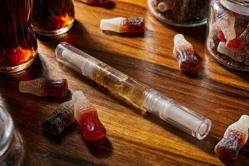 Clear scented cuticle oil pen in 3ml size on a wooden surface with cola bottles and gummies. Australian- made nail serums