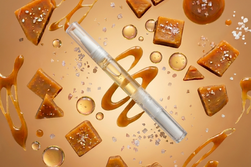 clear scented salted caramel cuticle oil pen with caramel pieces and syrup on a gold background
