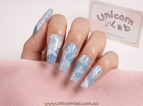 Nails with cloud design held by a hand, branded 'Unicorn Lab' in the background. waterslide nail decals Australia