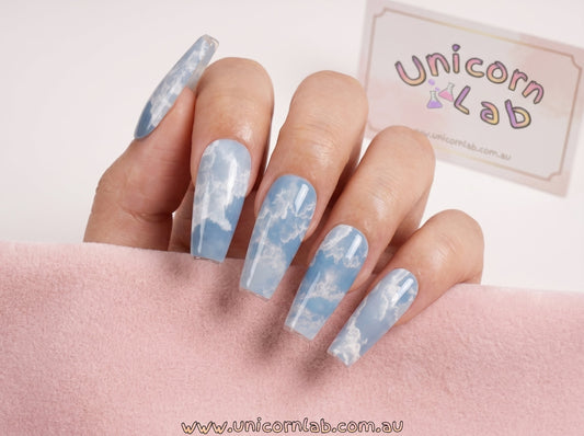 Nails with cloud design held by a hand, branded 'Unicorn Lab' in the background. waterslide nail decals Australia