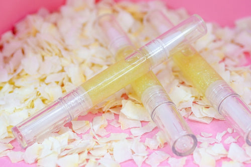 Three clear cuticle oil tubes filled with sparkling pale yellow serum, arranged on a bed of white flower petals against a bright pink background.