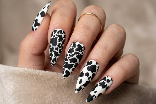 Hand with black and white cow print nails on a neutral background