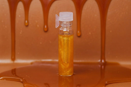 A small clear plastic vial filled with golden amber liquid, standing upright in a glossy caramel-like substance with dripping caramel above it.