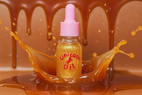 Bottle labeled 'Unicorn Oil' surrounded by splashes of orange liquid against a brown background