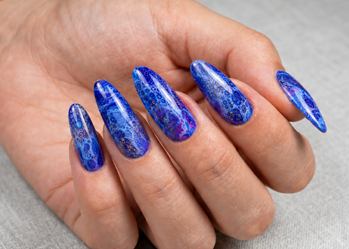 Hand with blue marbled nail polish on a neutral background