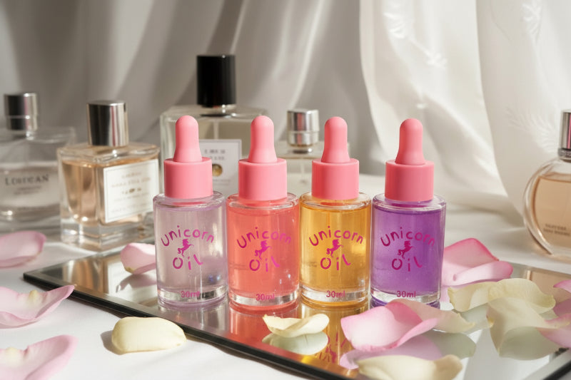 Four bottles of 'Unicorn Oil' with pink droppers on a reflective surface with flowers.