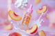 Bottle of 'Unicorn Oil' with peach slices and whipped cream on a pink background