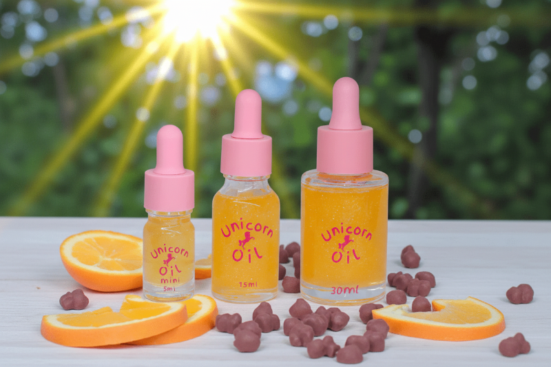 Jaffa Unicorn Cuticle Oil in 5ml 15ml and 30ml bottles with shimmery orange oil inside. Oils are surrounded by orange slices and chocolate