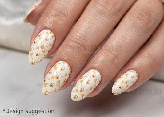 Close-up of a hand with white nail polish and gold bead embellishments on a neutral background.