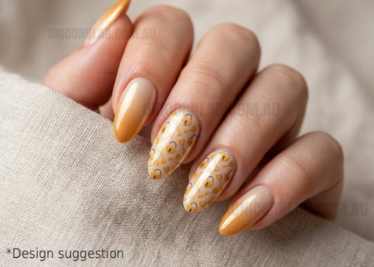 Hand with orange and gold gradient nails featuring a decorative pattern on a beige fabric background.