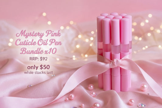 A bundle of ten pink cuticle oil pens tied with a pink ribbon, displayed on pink satin fabric with decorative pearls and fairy lights. Text on the left reads 'Mystery Pink Cuticle Oil Pen Bundle x10' with pricing details.