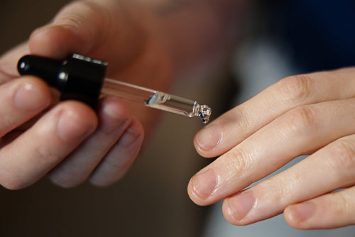 Close-up of a hand holding a small bottle with a dropper, likely containing a liquid.
