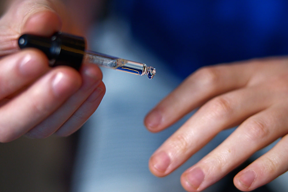 Close-up of a hand holding a small glass container with a black cap. a man applying cuticle oil