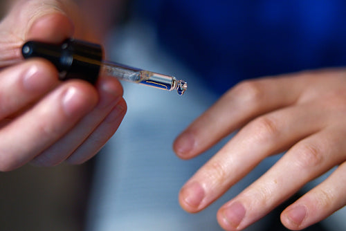 Close-up of a hand holding a small glass container with a black cap. a man applying cuticle oil