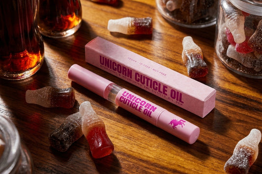Pink cola bottled scented cuticle oil pen with gummy candies on a wooden surface