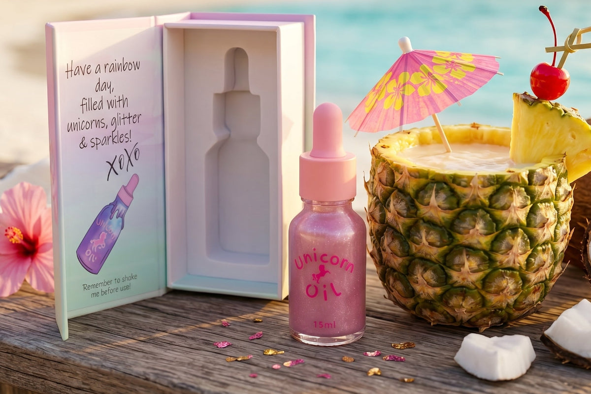 Unicorn oil bottle with dropper, gift box, pineapple with candle, and flowers on a wooden surface.