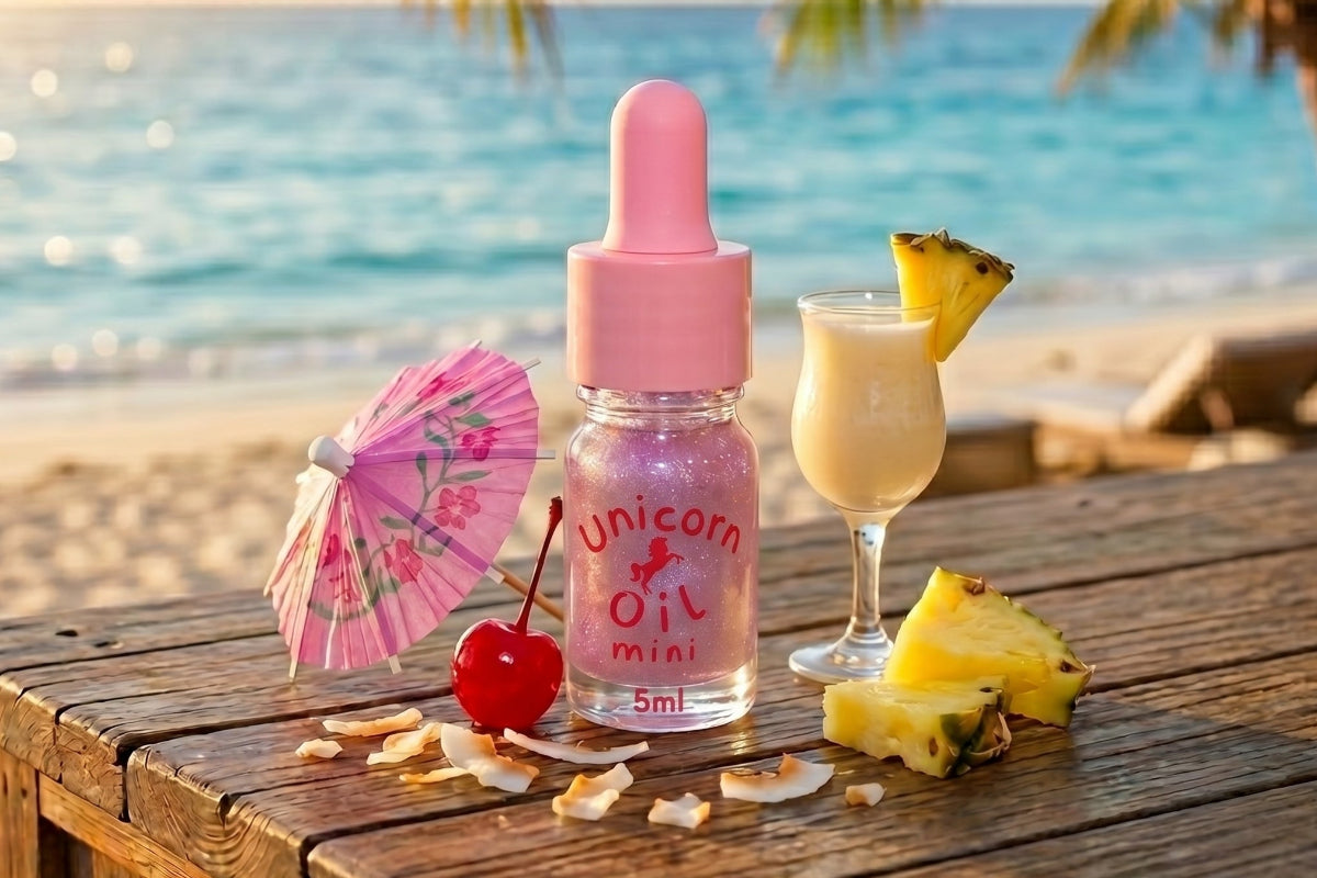 Pink bottle labeled 'Unicorn Oil Mini' on a wooden table with a tropical setting.