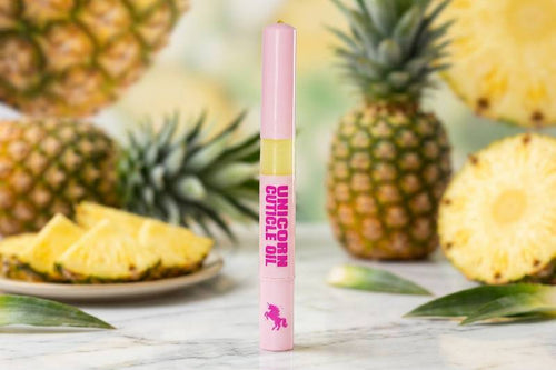 Pink and yellow cuticle oil pen with 'Unicorn Cuticle Oil' text on a marble surface with pineapples.