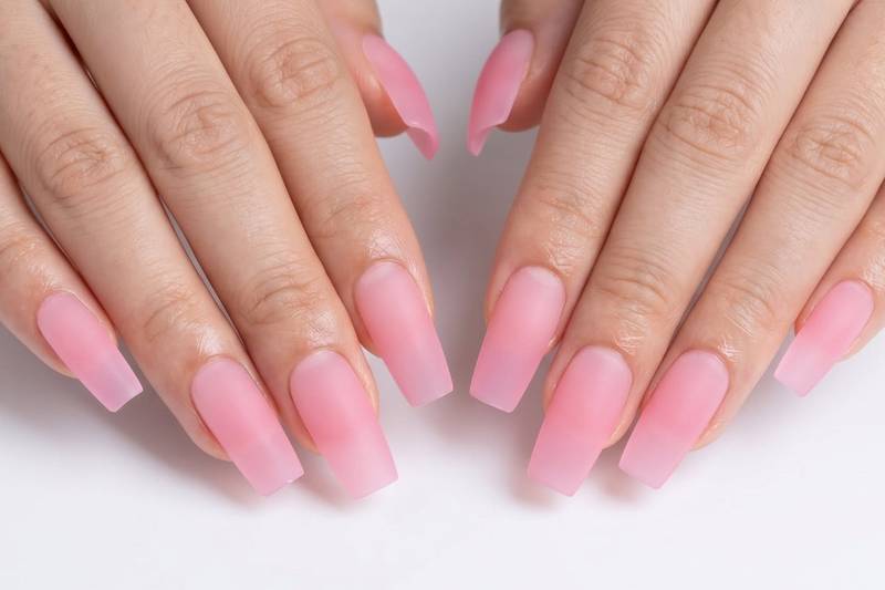 Close-up of hands with pink nail polish on a white background